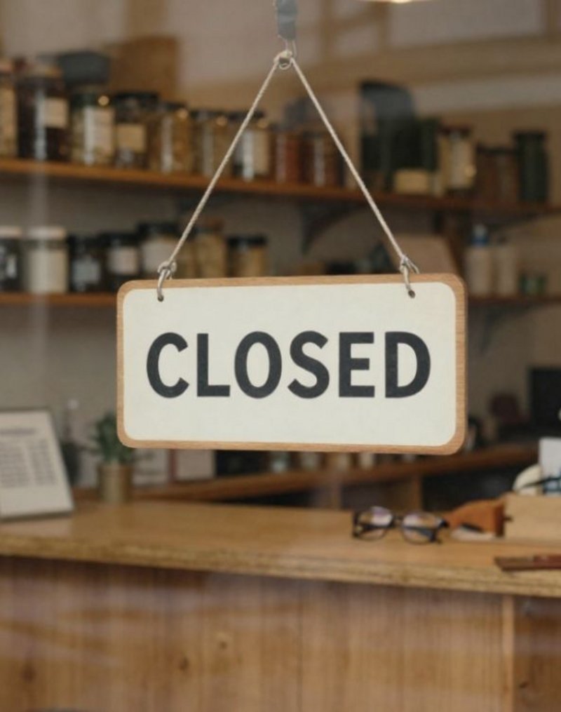 Geschlossener Laden von außen gesehen mit 'Closed'-Schild an der Tür, leere aber ordentliche Ladentheke im Inneren – Sinnbild für Unternehmensnachfolge